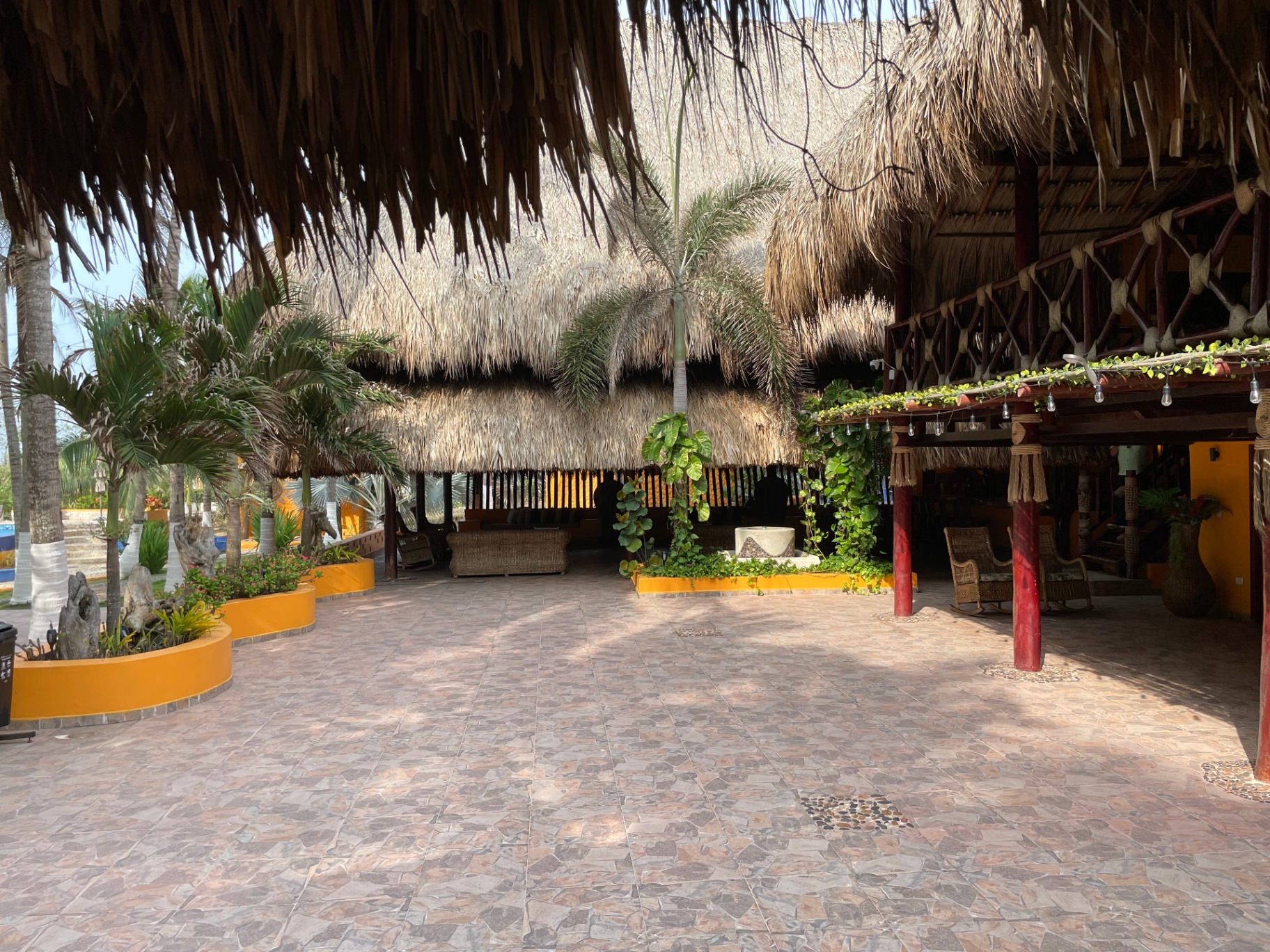 Patio interior bajo gran palapa con jardineras ocre y mobiliario en mimbre